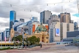 A photo overlooking Flinders Street Station from across Federation Square, on a slightly cloudy day.