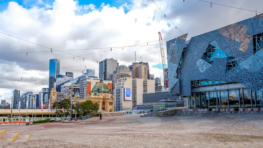 A photo overlooking Flinders Street Station from across Federation Square, on a slightly cloudy day.