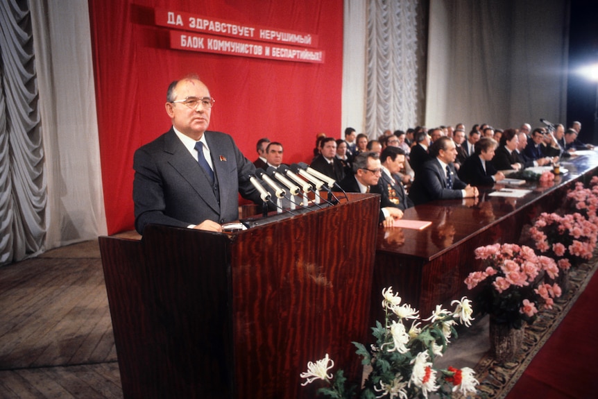 Archival photo of Mikhail Gorbachev standing behind a podium, addressing a crowd.