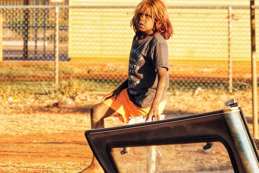 A child stands next to an old car roof.