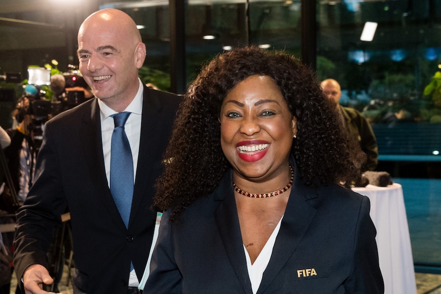 Two senior FIFA football executives - one male, one female - smile as they walk out of a press conference.