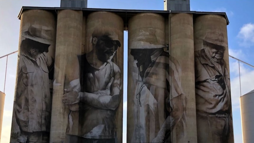 Four silos with a painting of a different farmer on each silo.