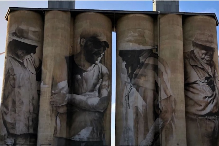 Four silos with a painting of a different hat-wearing farmer on each