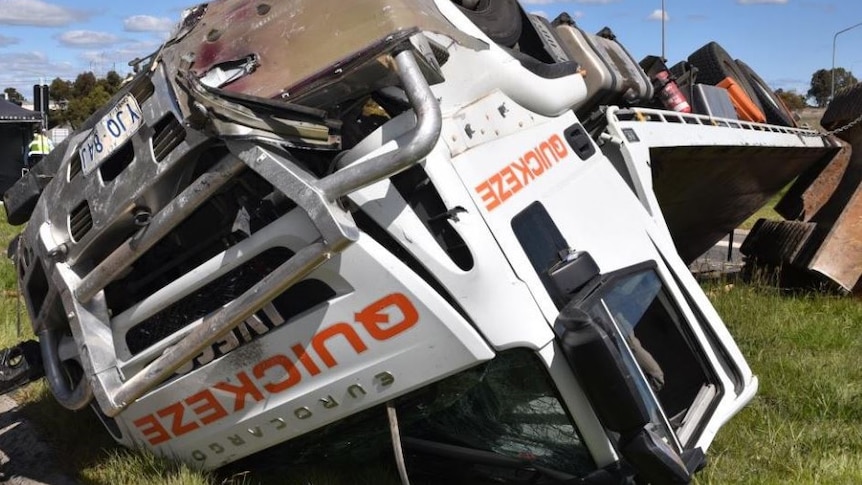 An upturned white truck lying on grass.