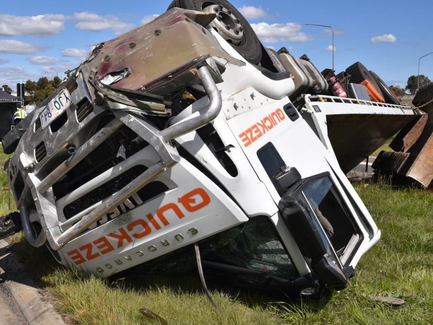 An upturned white truck lying on grass.