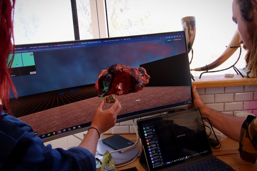 Looking at a computer screen with a big opal, holding a small opal (the same) in front of it. 