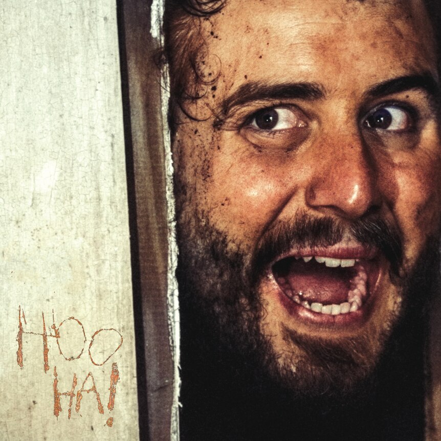 an unshaven man pokes his head around a door with his mouth open