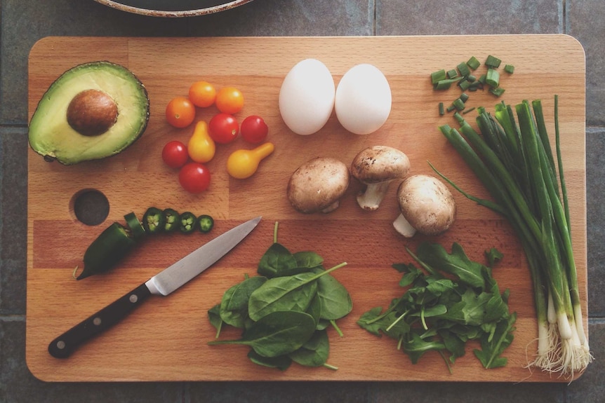 Chopping board with a knife, avocado, tomatoes, eggs, shallots, salad leaves and chilli