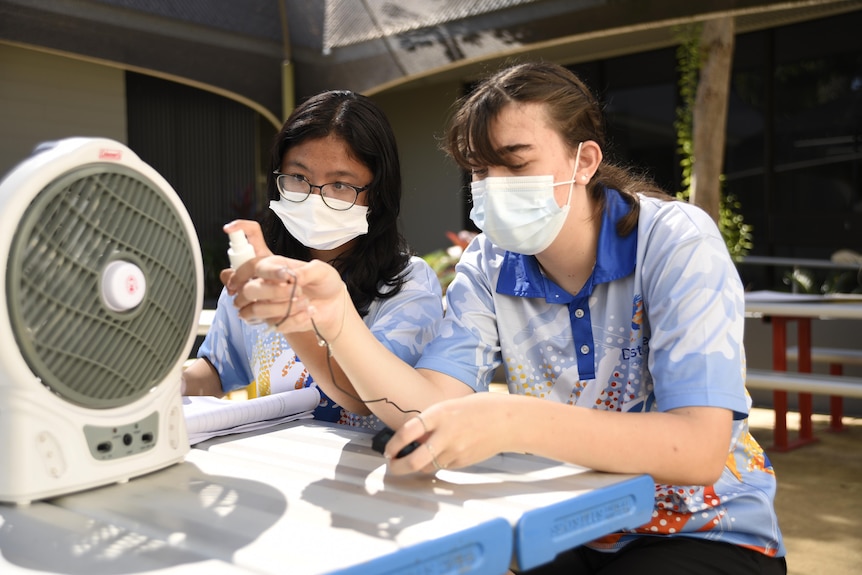 Two students carry out an experiment at a school using a fan and water.