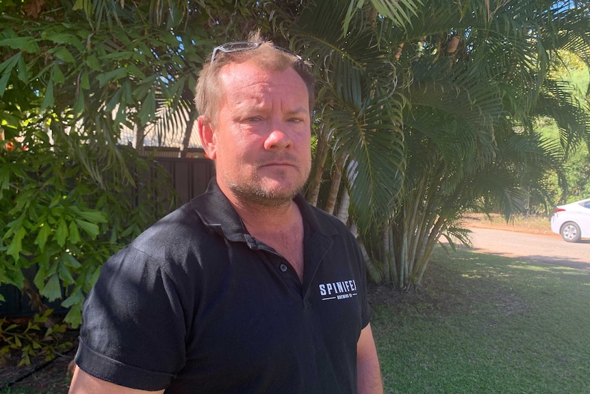 Image of a man in a dark blue shirt with white lettering standing at the side of a residential street in Broome.