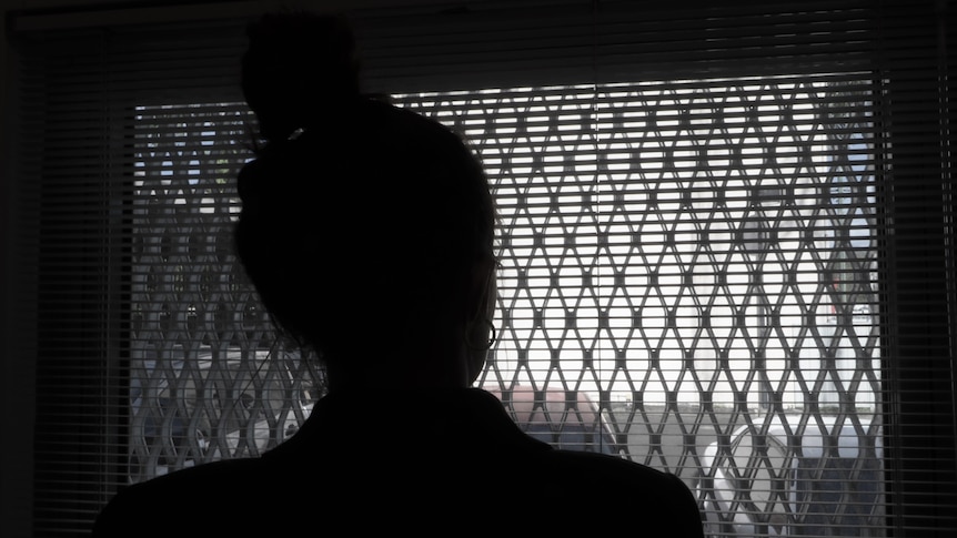 A silhouette of a woman as she looks out of a window