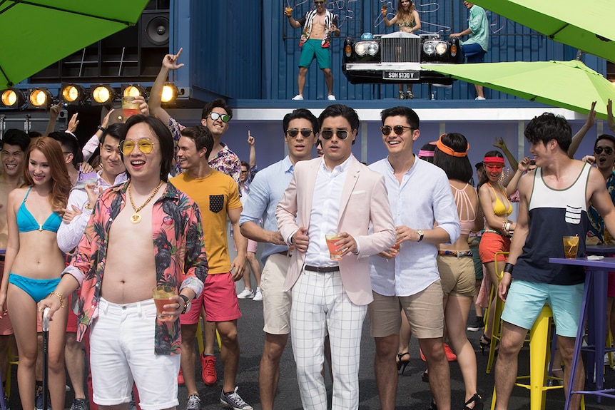 Still of actors Ronny Chieng, Chris Pang, Remy Hii and Henry Golding at an outdoor party scene in 2018 film Crazy Rich Asians.