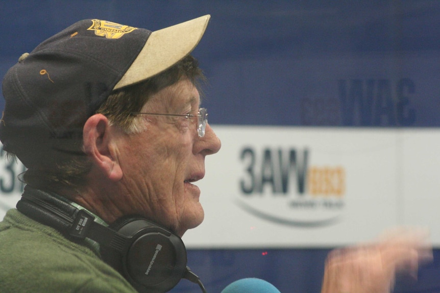 A man wears a baseball cap and headphones in a radio studio with a '3AW' banner in the background.