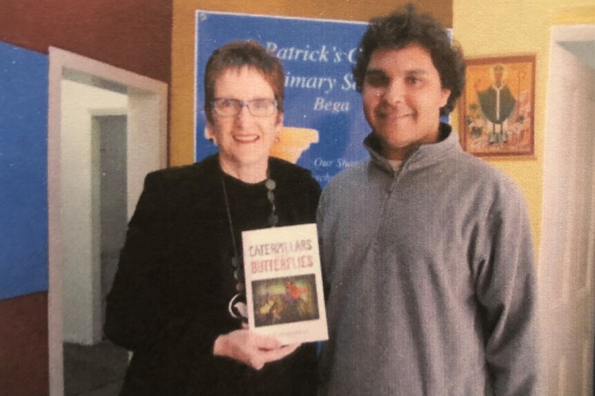 A teenage Gary smiles with Mrs Scott, holding his Caterpillars and Butterflies book.