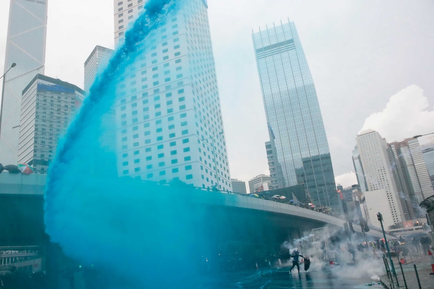 A wave of blue-coloured water cannon being sprayed onto protesters
