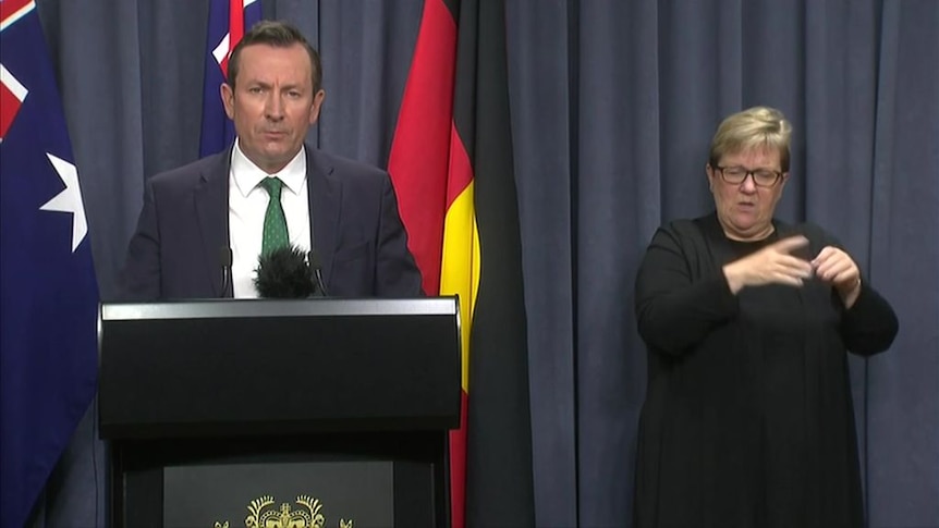 Mark McGowan talking during a media conference with a woman beside him performing sign language.