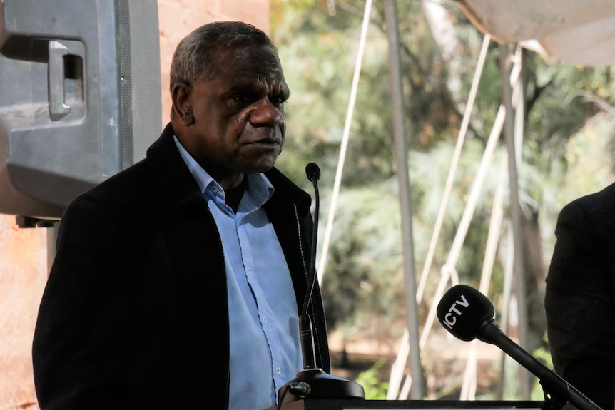 An Indigenous man stands behind a podium while making a speech