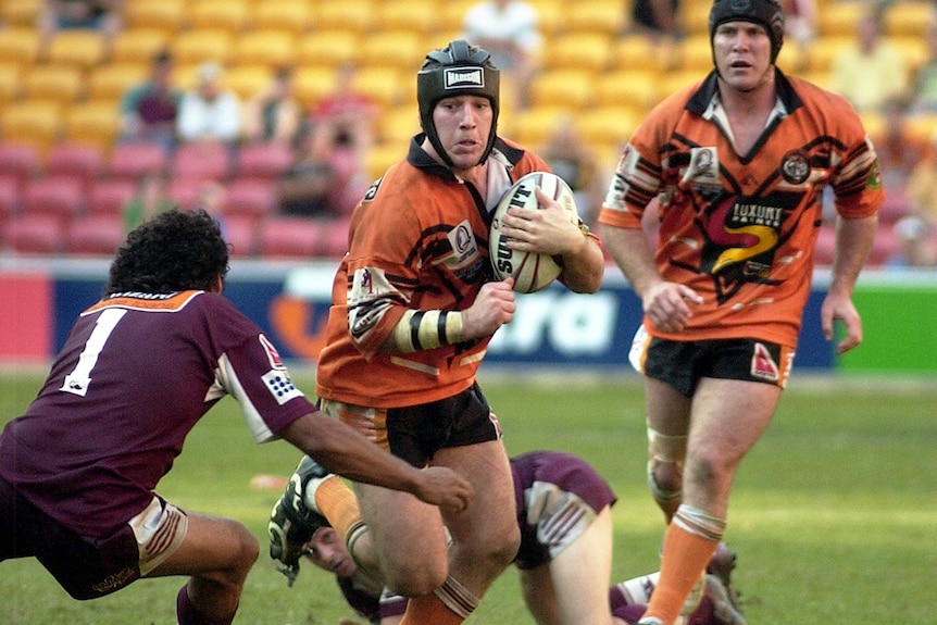A football player in orange tries to dodge his opposition in maroon