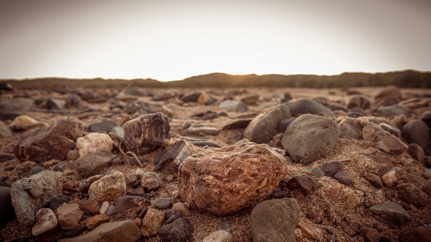 Red and brown rocks pictured on a sandy landscape in the Pilbara in Western Australia's north.