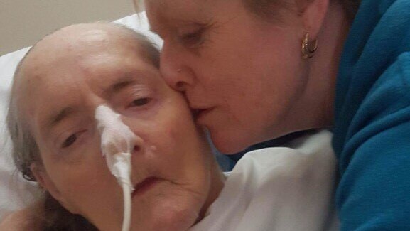 An older woman kisses her elderly, ill mother on the head.
