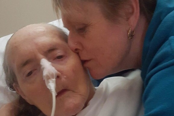 An older woman kisses her elderly, ill mother on the head.