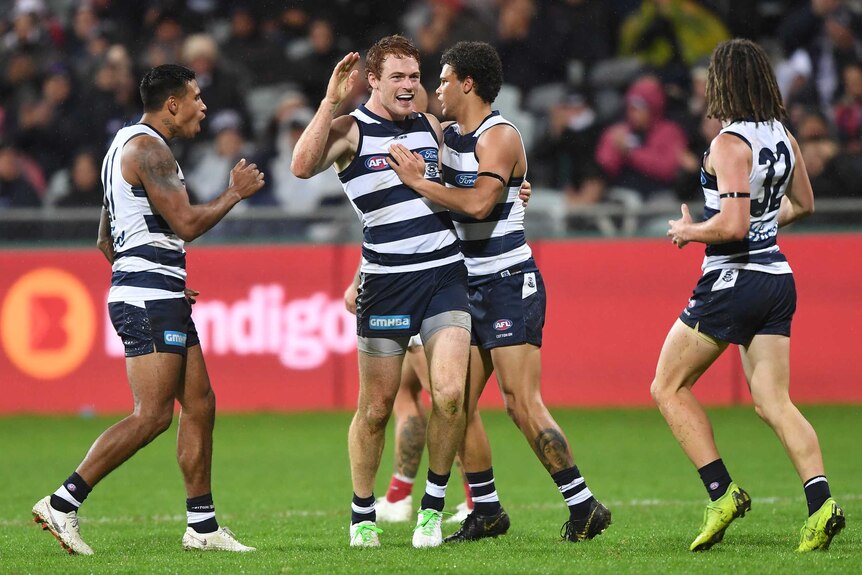 AFL players congratulate a goal-scorer who has his hand raised in acknowledgement.