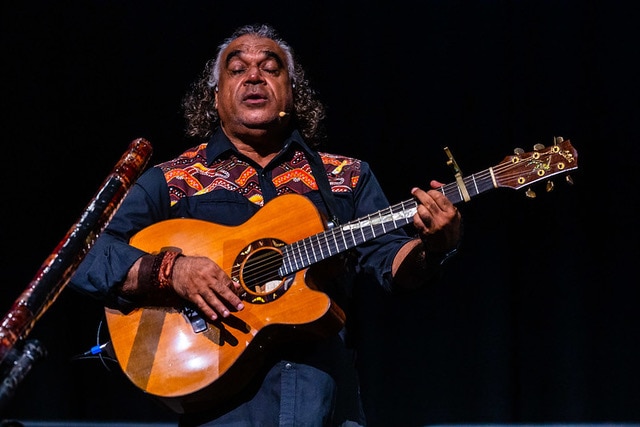 Cairns-based musician, artist and Indigenous tourism pioneer David Hudson plays a guitar on stage.