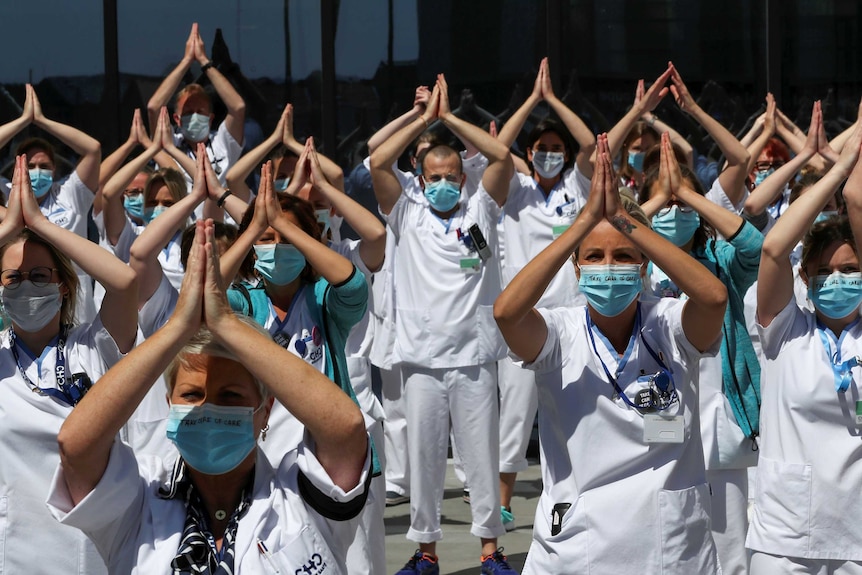 People lined up next to each other put their arms into a triangle shape in the air.