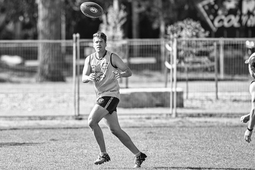 A man looks at a footy in anticipation of catching it while in a park.