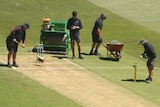 A number of groundspeople tend to a cricket pitch at the MCG.