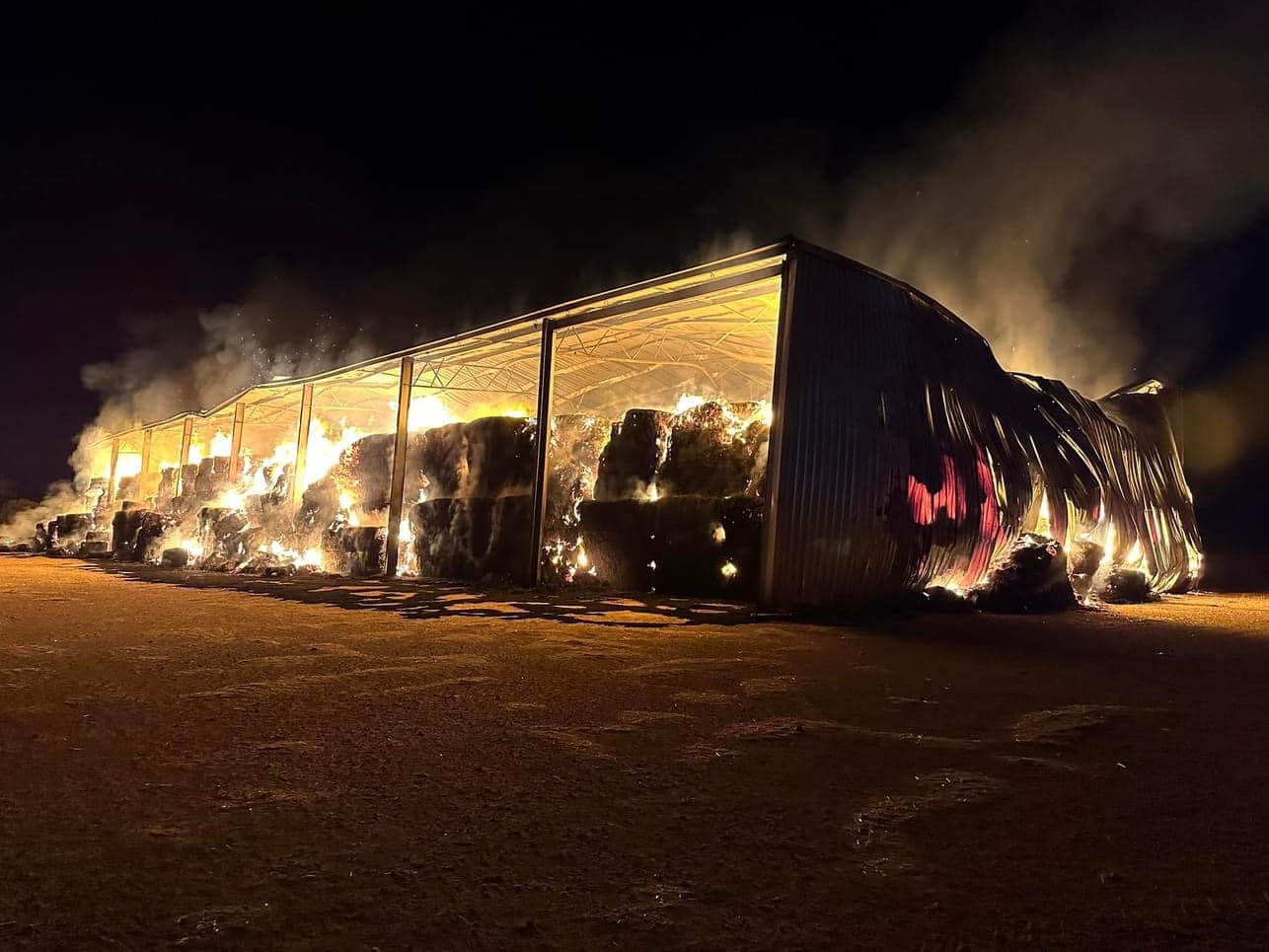 A shed with hay bales on fire at night.