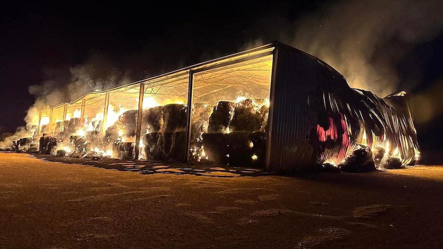 A shed with hay bales on fire at night.