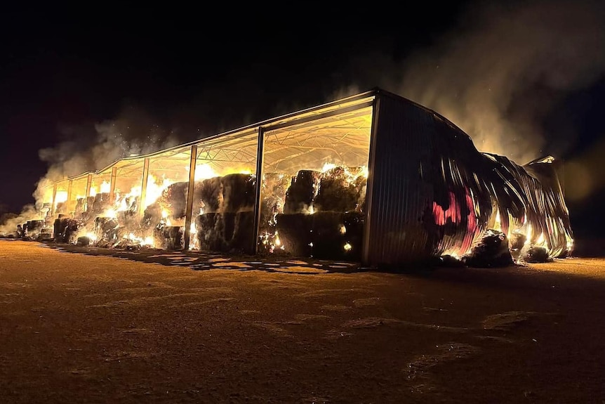 A shed with hay bales on fire at night.