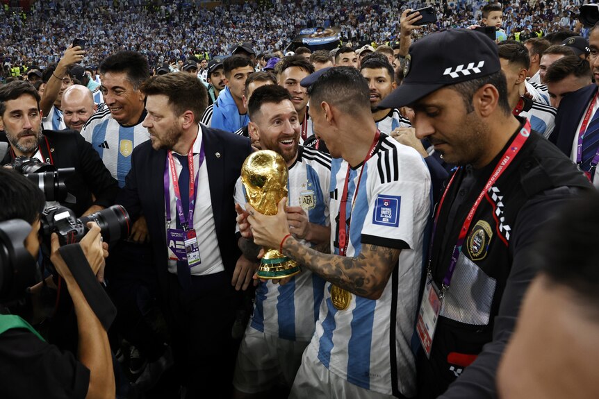 Argentina's Lionel Messi and Angel di Maria hold the FIFA World Cup trophy in a crowd of people after the Qatar final.