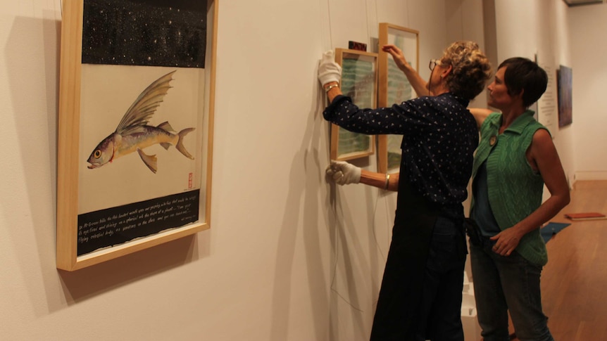 Two women hanging an artwork.