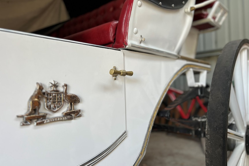 The coat of arms on a side of a cream horse carriage with gold handle