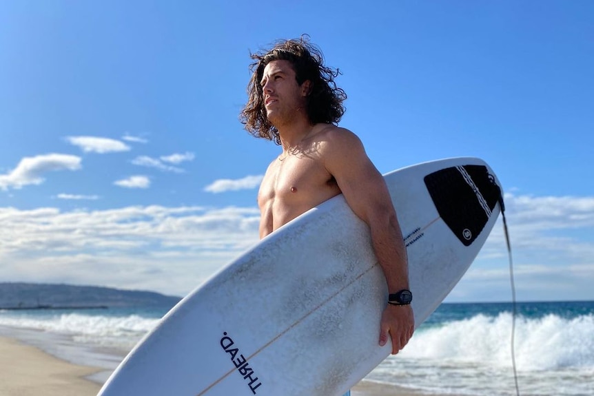 A man with long hair holds a surfboard