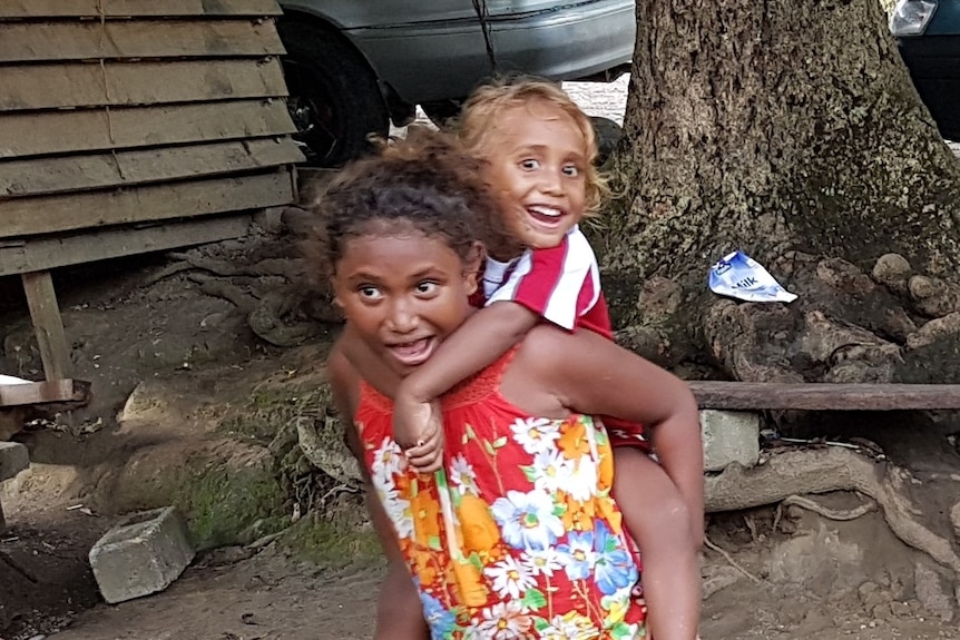 A young girl carries a toddler on her back