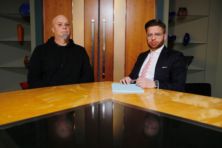 Two men sit at a long table.