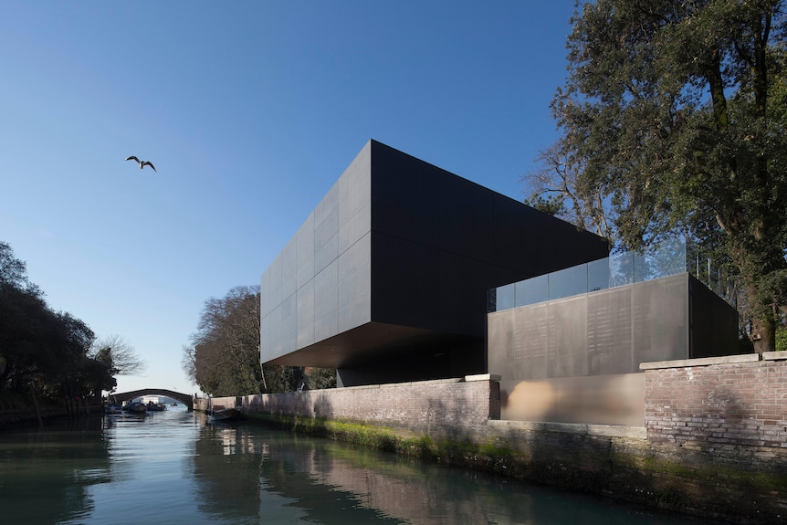 A black cube-like gallery building protrude over a canal in Venice.