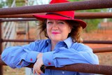A woman in a red hat leaning on a rusty bar of a gate.
