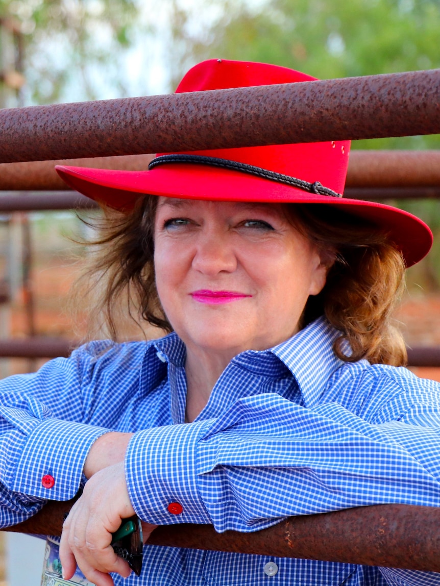 A woman in a red hat leaning on a rusty bar of a gate.