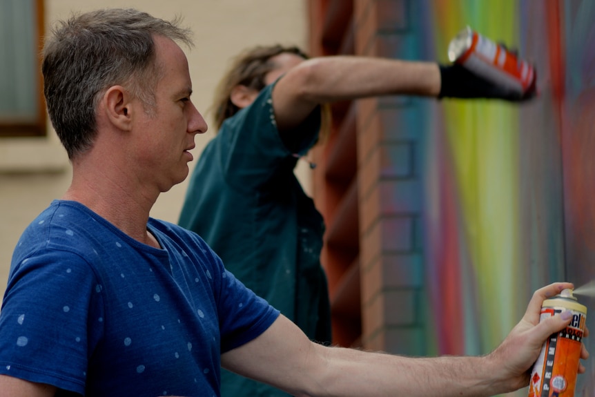 Side profile of James Cochran as he works on art on a wall.