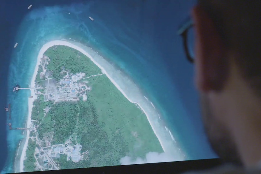 Someone with glasses looking at a large picture of an island with construction on it