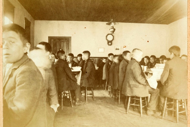 Young boys eat at a Native American boarding school dining hall.
