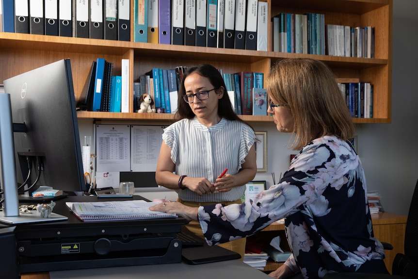 Two women sitting at a desk in an office looking at a notepad