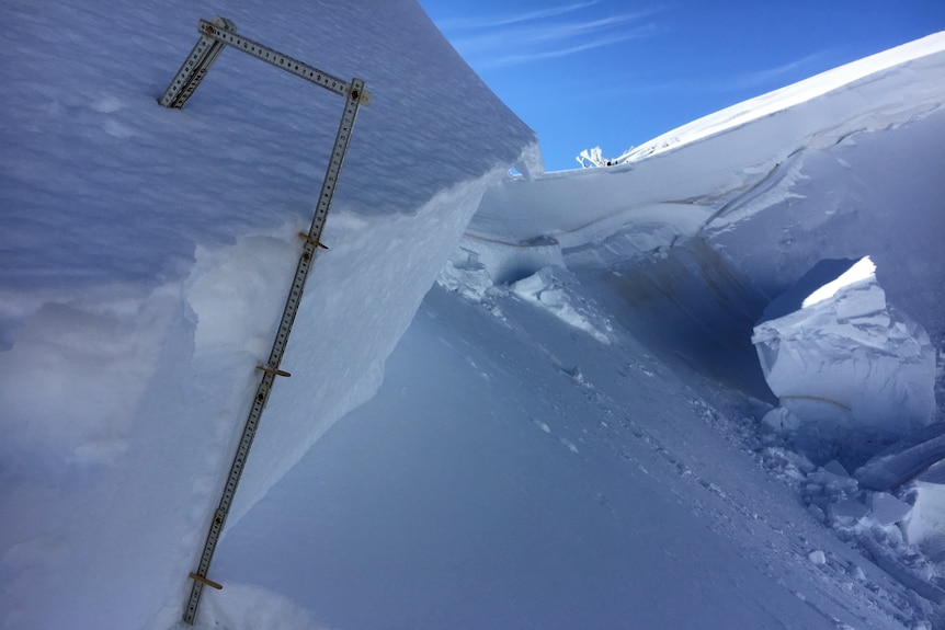 A stick measures the amount of snow that collapsed from a ledge.