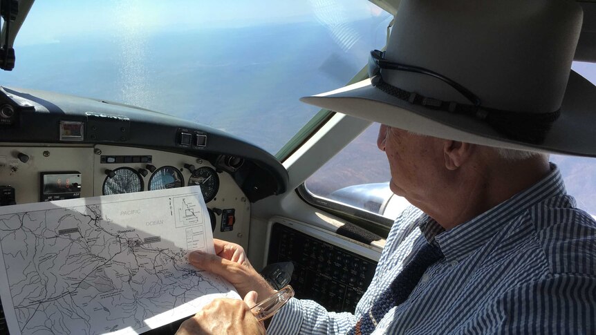 Bob Katter looks at a map while sitting in a small plane.