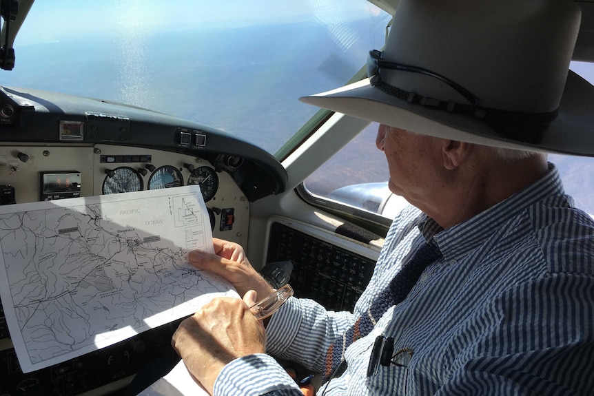 Bob Katter looks at a map while sitting in a small plane.