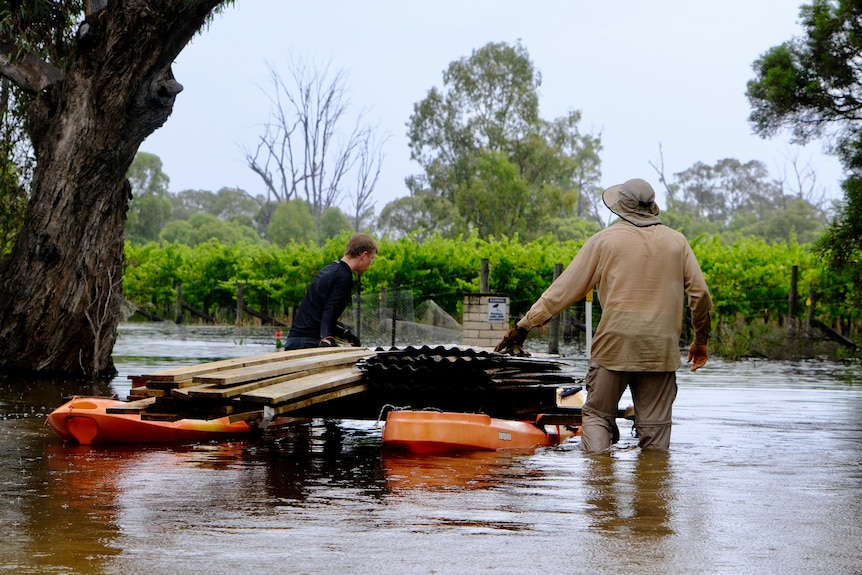 Two men push along two canoes tied together with metal and wooden beams on it